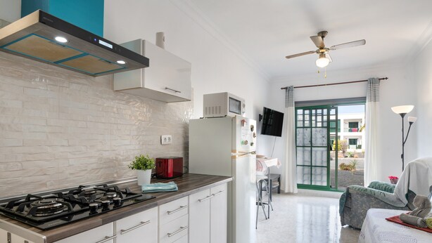 Eine moderne Küche mit Gasherd, weißen Schränken, einer Mikrowelle und einem Deckenventilator.