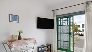 Ein Zimmer mit Tisch, Stühlen, einem Fernseher, einem Fenster mit Vorhängen und einer Tür mit grünem Rahmen.