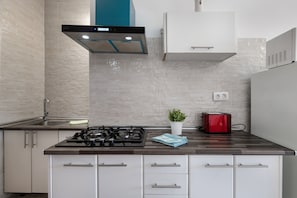 Une cuisine moderne avec une cuisinière à gaz, des armoires blanches, un grille-pain rouge et une plante en pot.