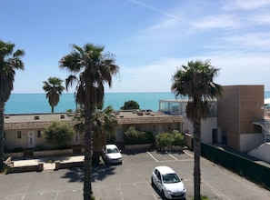 Un aparcamiento con dos coches, palmeras y un edificio con vistas al mar.