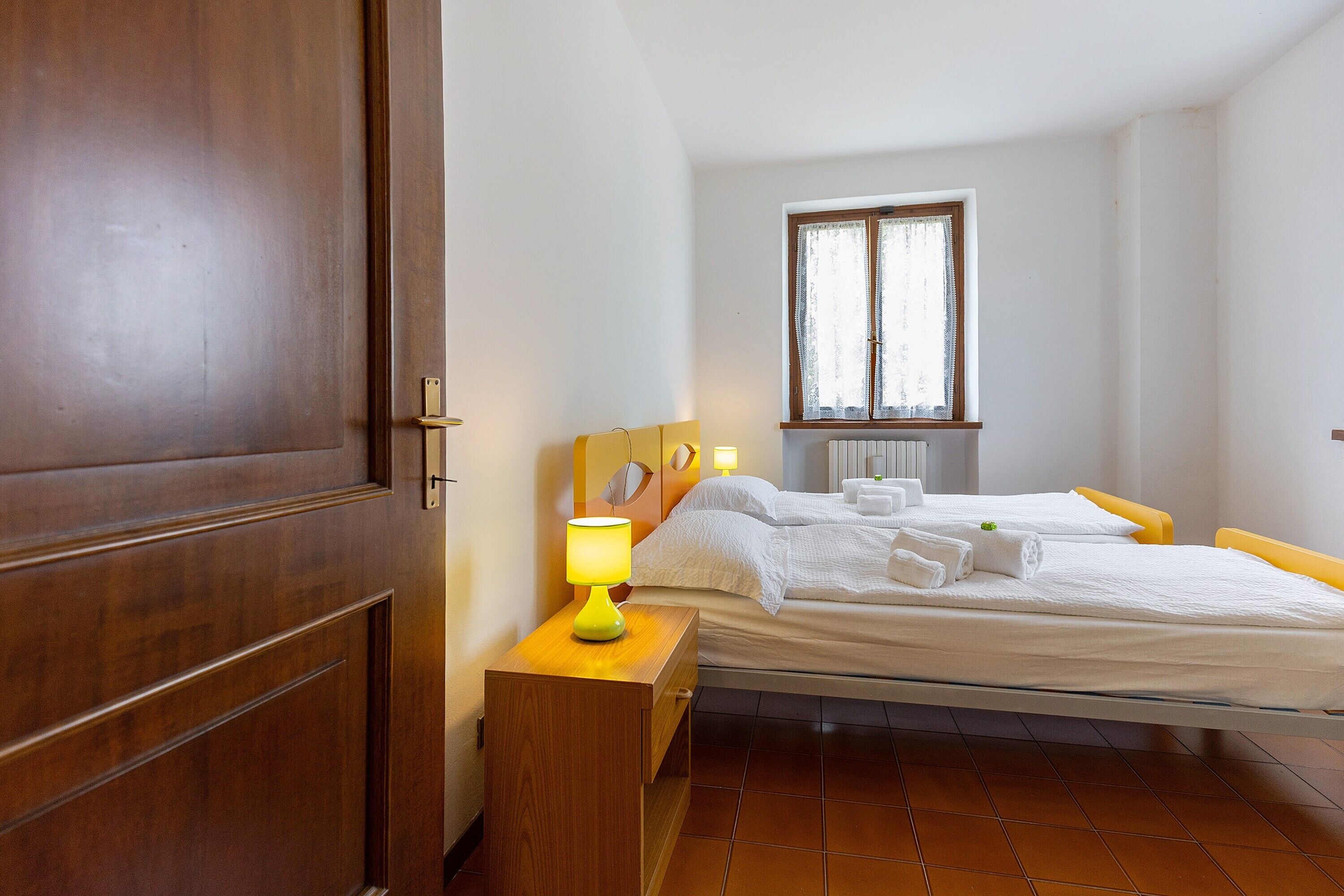 Una camera da letto con un letto, un comodino con una lampada, una finestra e una porta.