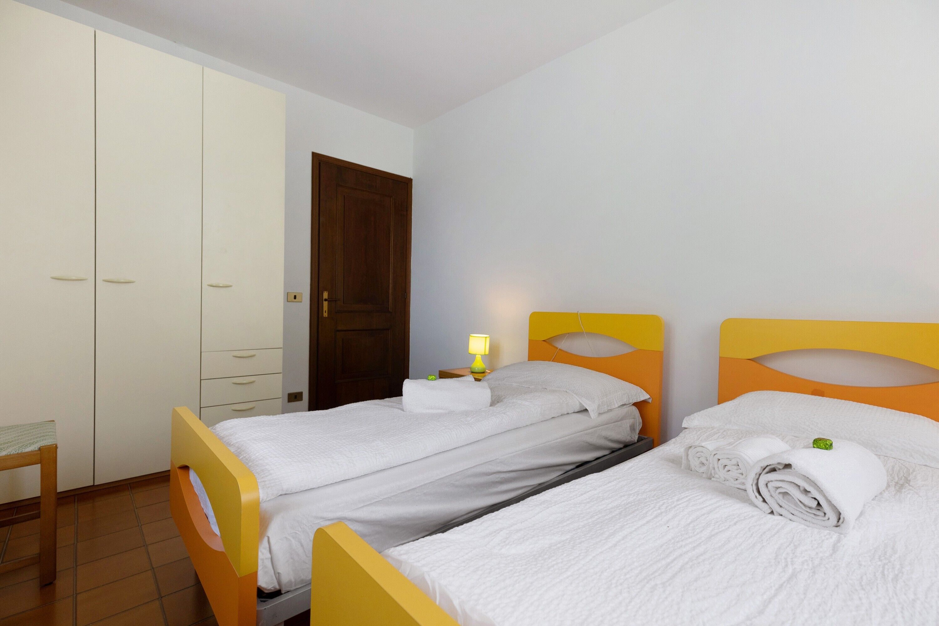 Ein Zimmer mit zwei Betten, einem Kleiderschrank, einer Tür und einem Nachttisch mit Lampe.