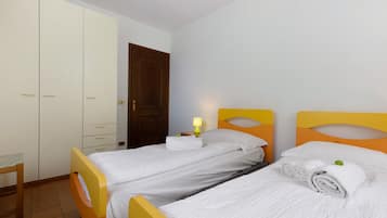 Ein Zimmer mit zwei Betten, einem Kleiderschrank, einer Tür und einem Nachttisch mit Lampe.