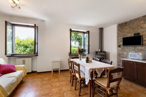 A dining area with a table set for four, a sofa, a stone wall, a fireplace, and a TV mounted on the wall.