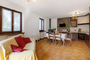 A living room with a sofa, a dining table with chairs, a kitchen area with a stove, and a stone wall.