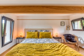 Une chambre à coucher avec un lit, deux lampes de chevet, un fauteuil en osier et une fenêtre.