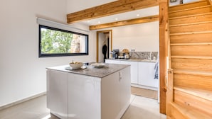 A modern kitchen with a central island, wooden beams, and a view of the outdoors. - Le Mas De Coeur with Mountain View, Wi-Fi and Air Conditioning (Bédarieux)