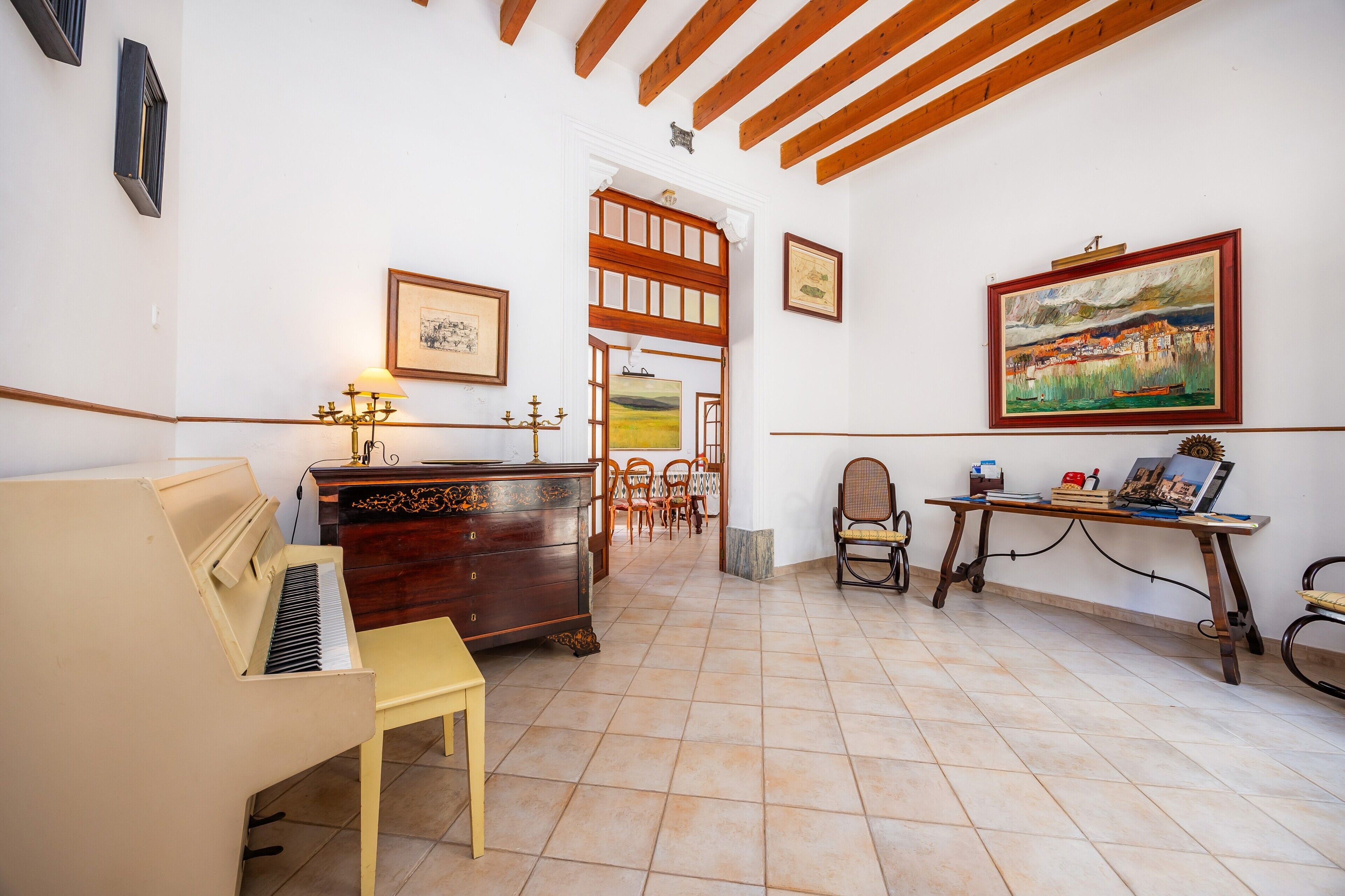 A room with a piano, wooden furniture, a dining table, and artwork on the walls.