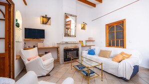 Ein Wohnzimmer mit Kamin, weißen Sofas, einem Fernseher und einer Holzbalkendecke.