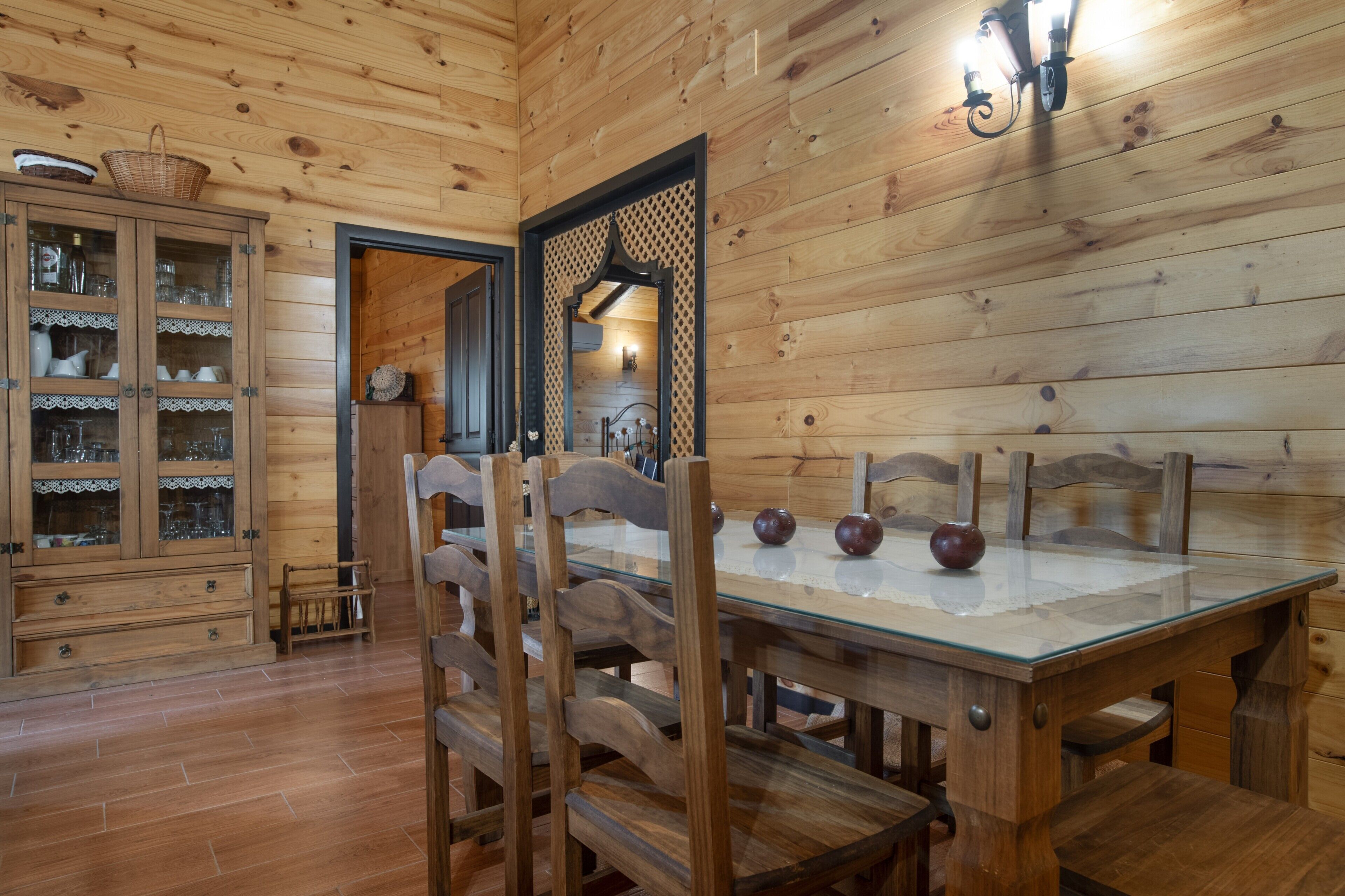 A wooden interior with a dining table, chairs, and a cabinet with glass doors.