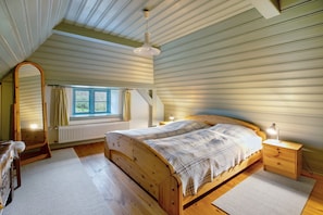 Une chambre à coucher avec un lit en bois, une table de chevet avec une lampe, une fenêtre avec des rideaux et un radiateur.