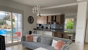 Un salón moderno con un sofá gris, una manta blanca y una cocina al fondo.