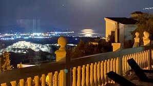 Un balcón con barandilla, una silla y vista panorámica de la ciudad de noche.