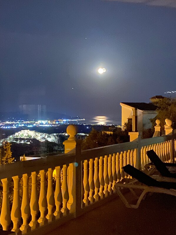 A balcony with a railing, a chair, and a view of a cityscape at night.