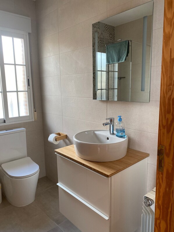 A bathroom with a toilet, a sink with a mirror, and a window.