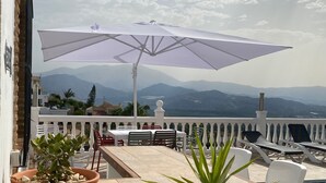 Una terraza con mesa, sillas, una sombrilla y vistas a las montañas.