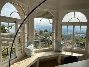 A room with large arched windows, a white desk, and a view of a mountainous landscape.