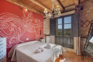 A bedroom with a large bed, a stone wall, a wooden ceiling, and a window with a view.