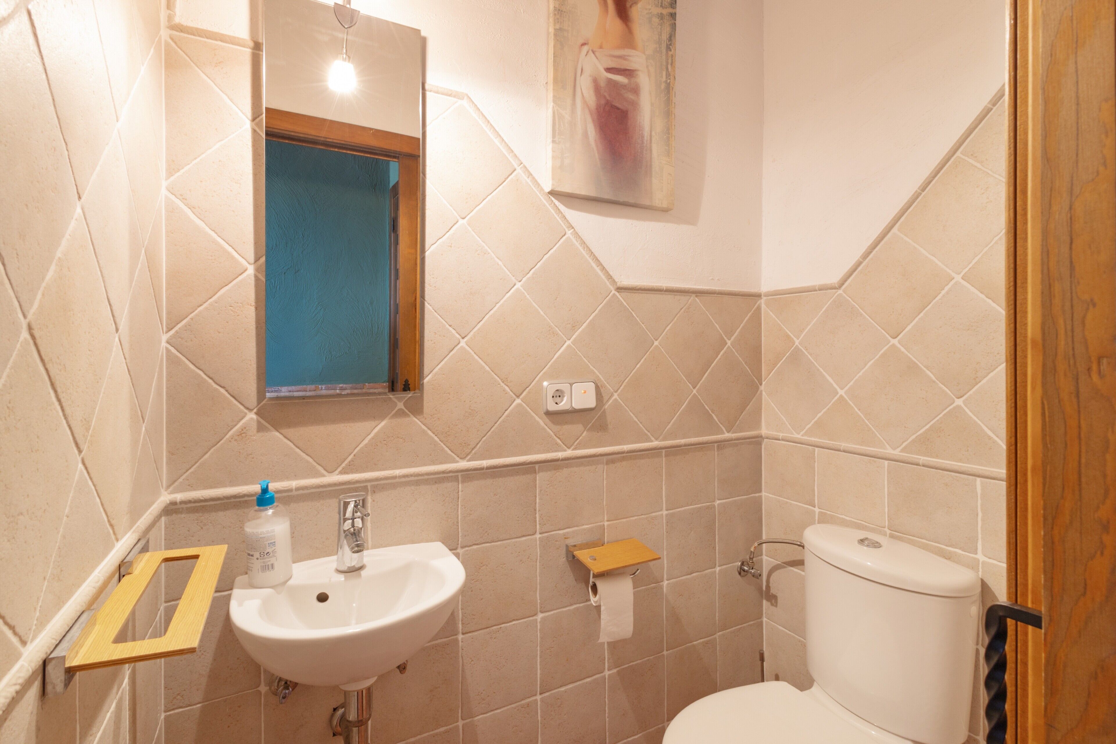 Ein Badezimmer mit Waschbecken, Spiegel, Toilette und einer kleinen Holzablage.