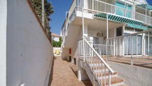 Un edificio con fachada blanca, un sendero de baldosas y una escalera que lleva a un balcón con toldos a rayas.