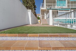 Un chemin menant à un bâtiment à l’extérieur blanc et aux accents bleus, avec une pelouse verte et une bordure carrelée.