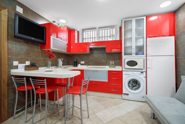 Une cuisine moderne avec des meubles rouges et blancs, un lave-linge encastré et un téléviseur à écran plat fixé au-dessus du plan de travail.