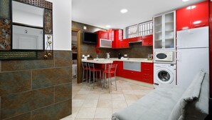 Cocina compacta con armarios rojos, lavadora integrada y zona de comedor con taburetes.