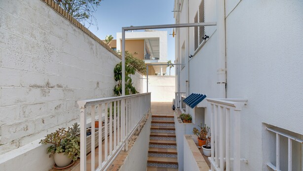 Un estrecho pasillo exterior con barandilla blanca, escalones con azulejos y macetas.
