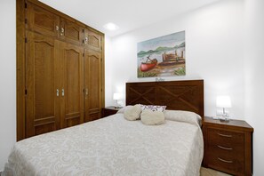 Une chambre avec une grande armoire en bois, un lit avec une literie à motifs, une table de chevet avec une lampe et un tableau représentant un bateau accroché au mur.