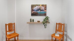 A room with two wooden chairs, a wooden shelf with a plant, a cactus, and a bowl, and a wall-mounted picture of a waterfall. - Tomasol Vacation Apartment with Sea Views, Private Terrace, and Wi-Fi (Los Cristianos)