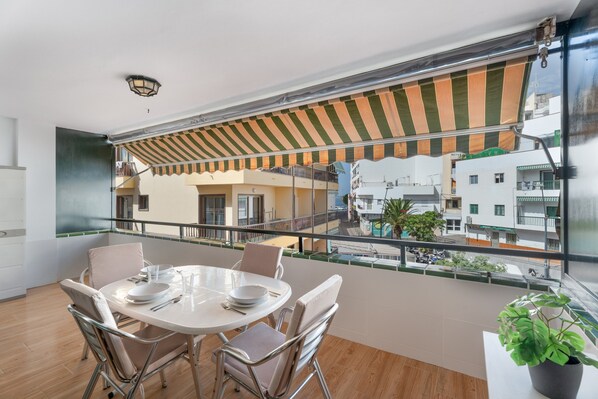 A balcony with a striped awning, a dining table with chairs, and a potted plant.