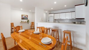 A dining area with a wooden table and chairs, a kitchen with white cabinets, and a small plant on the wall. - Tomasol Vacation Apartment with Sea Views, Private Terrace, and Wi-Fi (Los Cristianos)