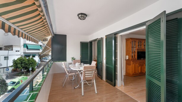 A balcony with a table and chairs, a view of the street, and a door leading to a room with a cabinet. - Tomasol Vacation Apartment with Sea Views, Private Terrace, and Wi-Fi (Los Cristianos)