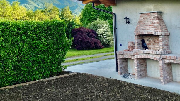 A brick-built outdoor fireplace with a chimney, surrounded by a well-maintained garden and a view of mountains. - Villa Giulia - Marguareis (Piemonte)