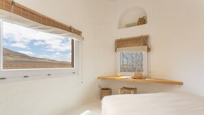 Un dormitorio con un ventanal grande, una cama, un estante de madera y un pequeño ventanal en forma de arco sobre el estante.
