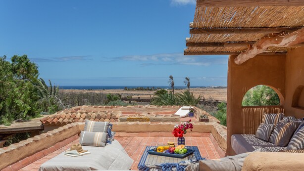 Una terraza con mobiliario exterior, una mesa con frutas y flores, y vistas del paisaje.