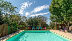 Ein rechteckiger Swimmingpool mit klarem Wasser, umgeben von einer Holzterrasse und Bäumen.