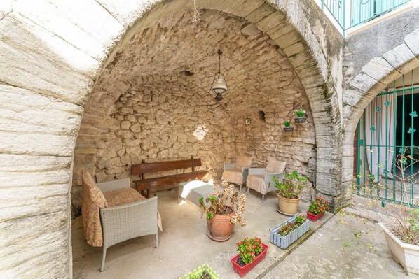 Un espace extérieur aménagé avec des murs en pierre, des meubles en osier et des plantes en pot.
