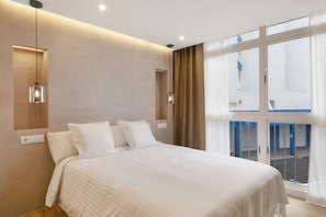 Quarto de hotel moderno com uma cama grande, vista através de uma porta de vidro e iluminação pendente.