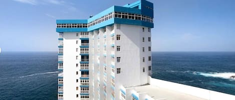 A high-rise hotel with multiple floors, a prominent blue and white color scheme, and a view of the ocean.