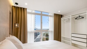 Ein Hotelzimmer mit Bett, Kleiderschrank, Pendelleuchte und einem fenster mit Vorhängen.