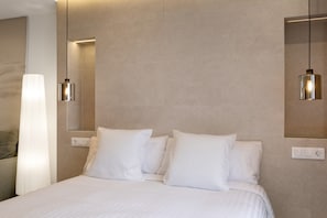 Une chambre d’hôtel avec un grand lit, deux lampes de chevet, un luminaire fixé au mur et une prise de courant.