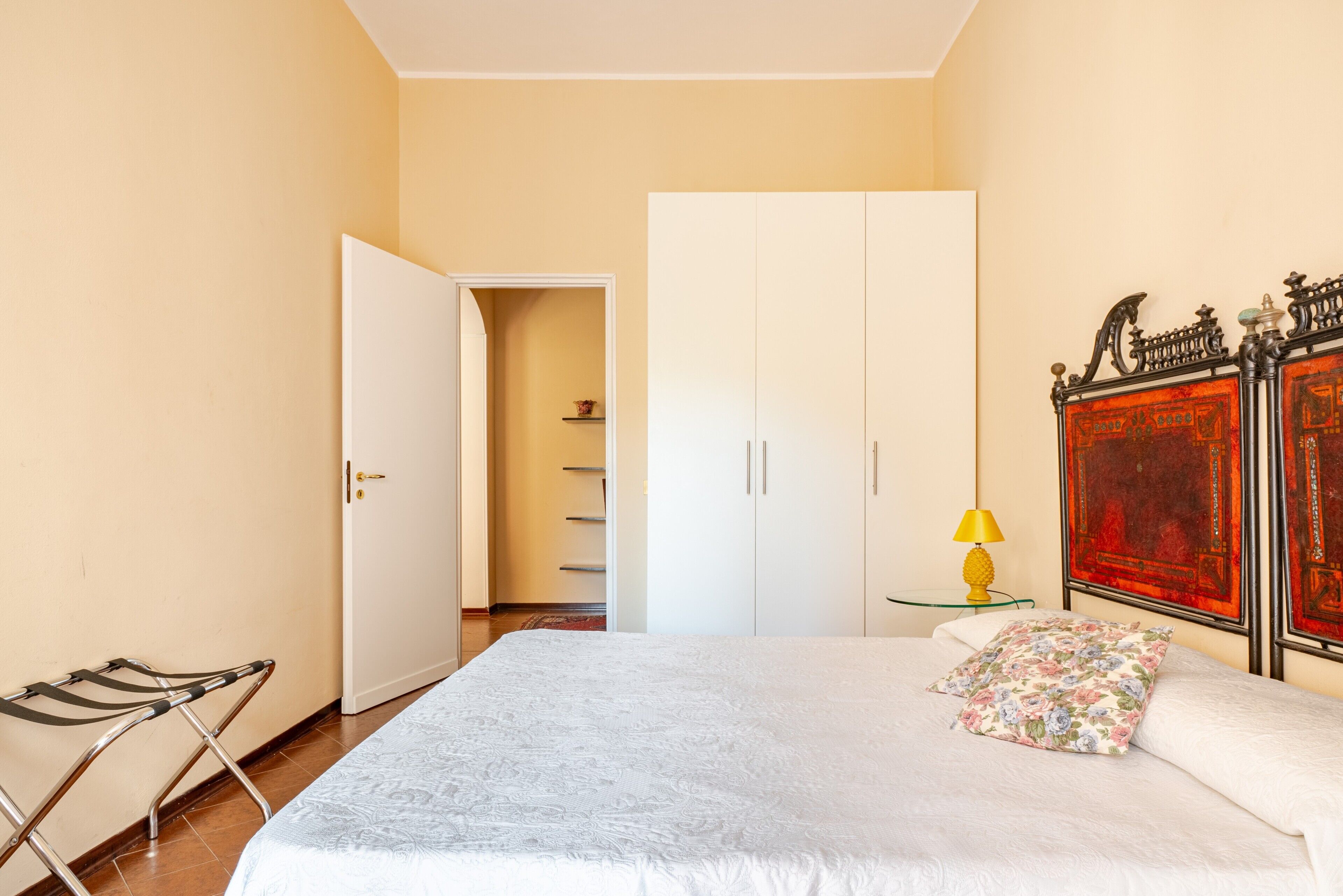 A bedroom with a bed, a wardrobe, a bedside table with a lamp, and a shoe rack.