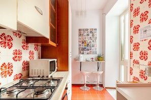 Une cuisine équipée d’une cuisinière à gaz, d’un four à micro-ondes et d’un mur recouvert de carreaux décorés de motifs floraux rouges.