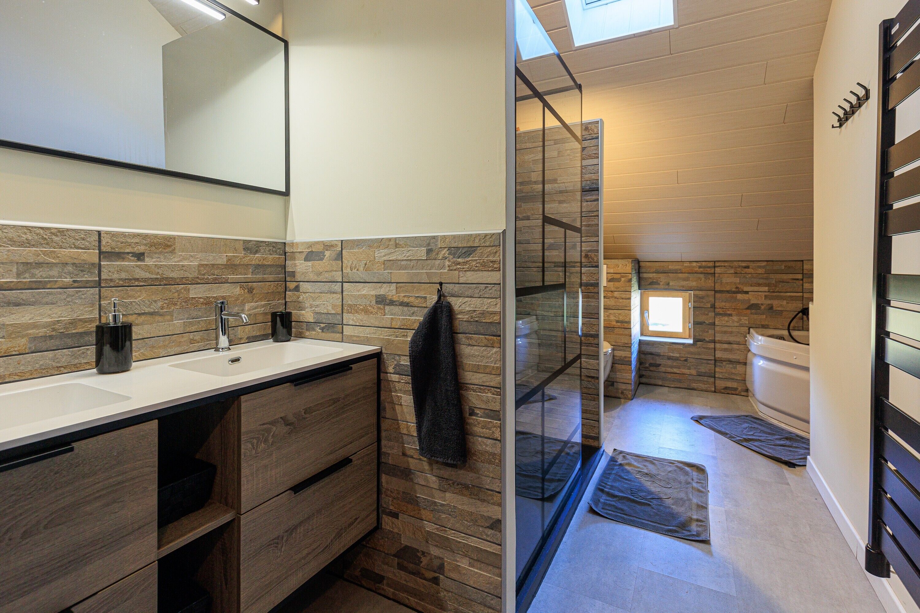 Une salle de bain moderne avec un mur en pierre derrière le lavabo, une douche en verre et un meuble-lavabo en bois avec un miroir.