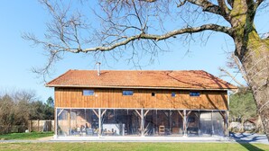 Un edificio de madera con techo de tejas, grandes ventanales y un patio con césped.