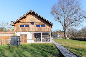 A wooden house with a covered patio, a fenced yard, and a gravel path.