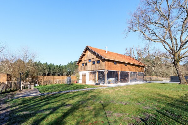Ein Holzhaus mit einem großen Glasanbau, umgeben von einem eingezäunten Garten und Bäumen.