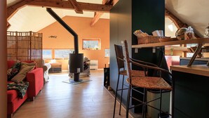 Una sala de estar acogedora con chimenea, vigas de madera, un sofá y una zona de comedor con sillas.