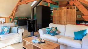 Un salón tipo loft con vigas de madera a la vista, chimenea, sofás blancos con cojines de colores y una mesa de centro de madera.